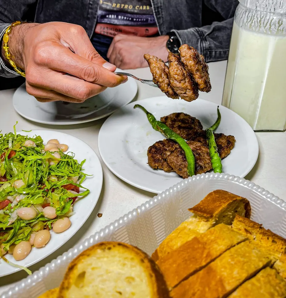 Çatalda ızgara köfte; yanında piyaz, közlenmiş biber, ekmek ve ayran