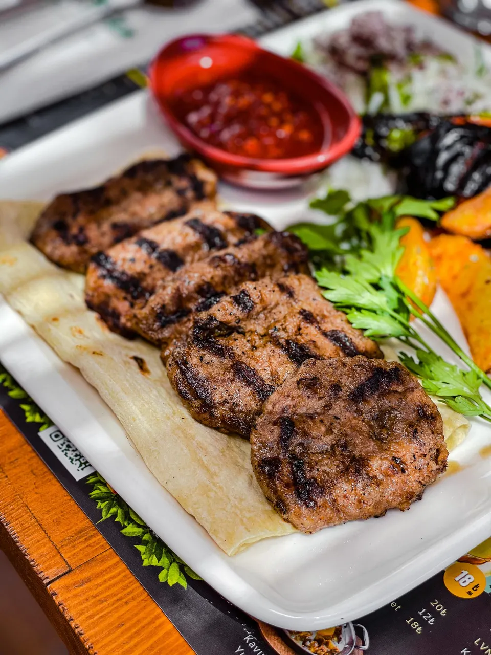 Lavaş üzerinde ızgara köfte, patates ve acı sos